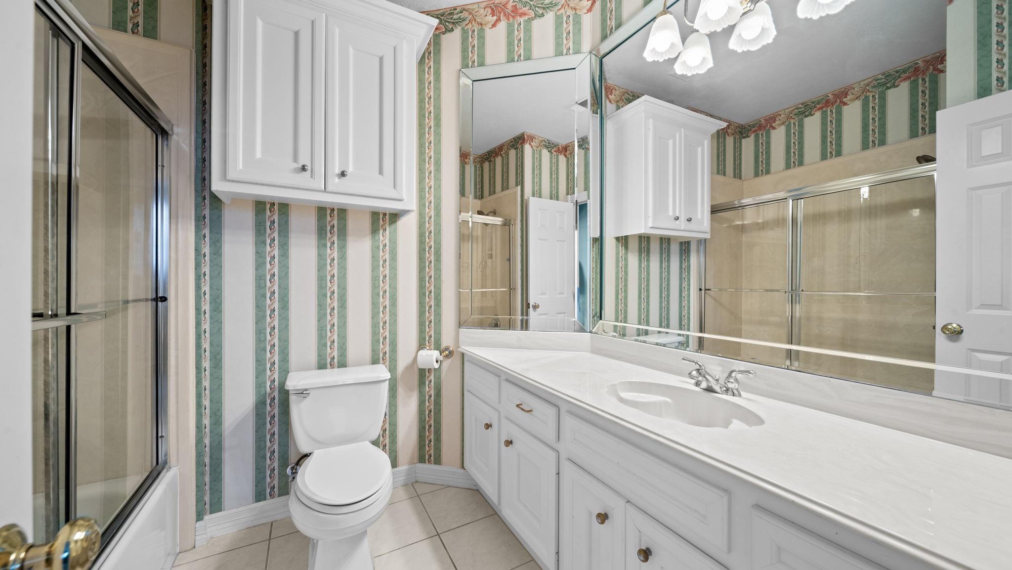 Bathroom with a long white vanity and mirrored wall, glass shower, and green striped wallpaper.