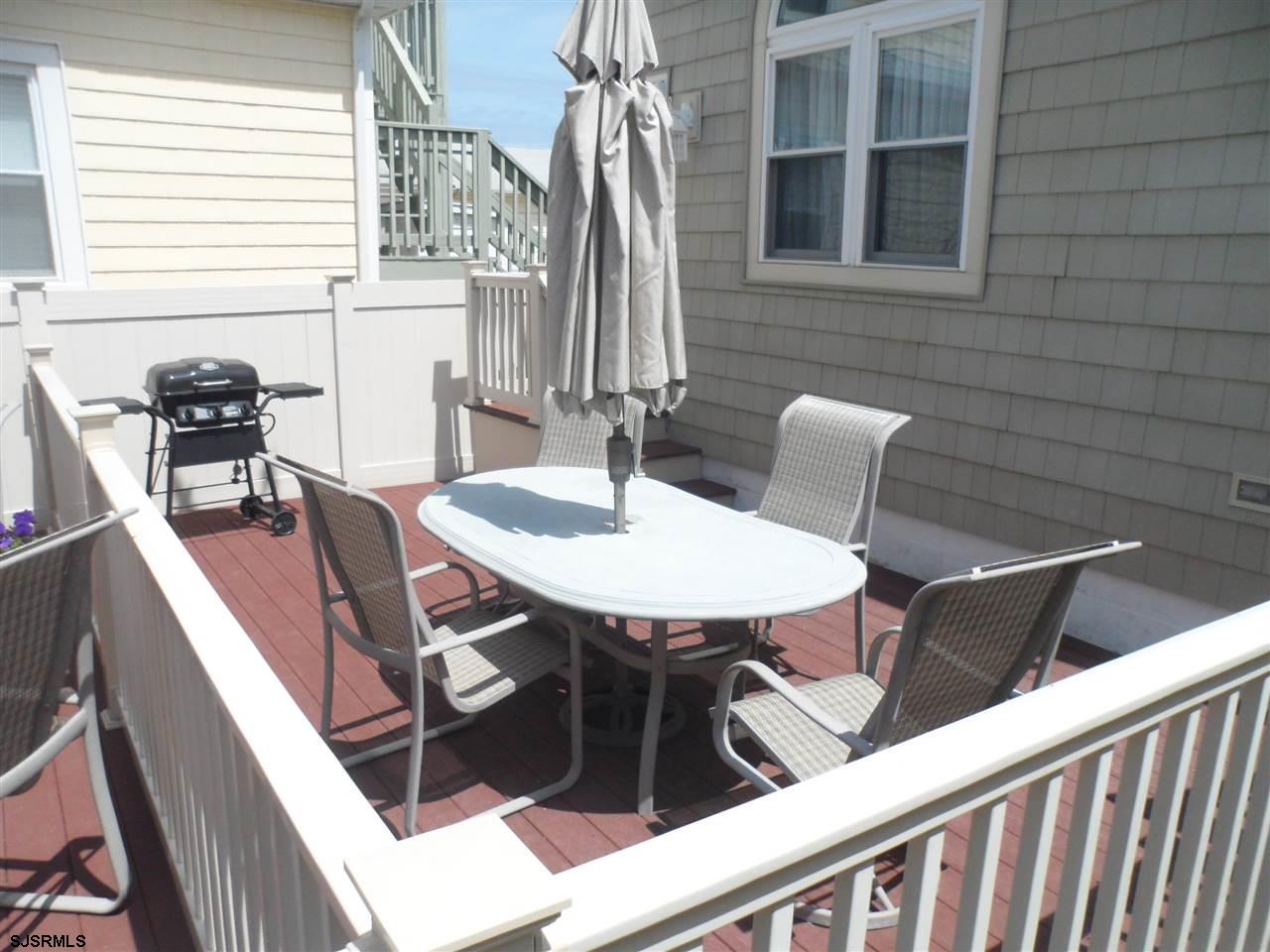 Raised deck with outdoor dining set, closed umbrella, and grill beside a shingle-sided home.