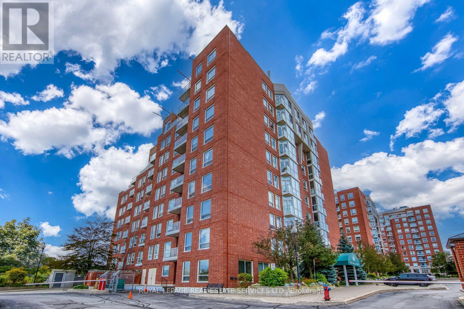 Red-brick condominium with glass balconies, viewed from below beneath a partly cloudy sky.