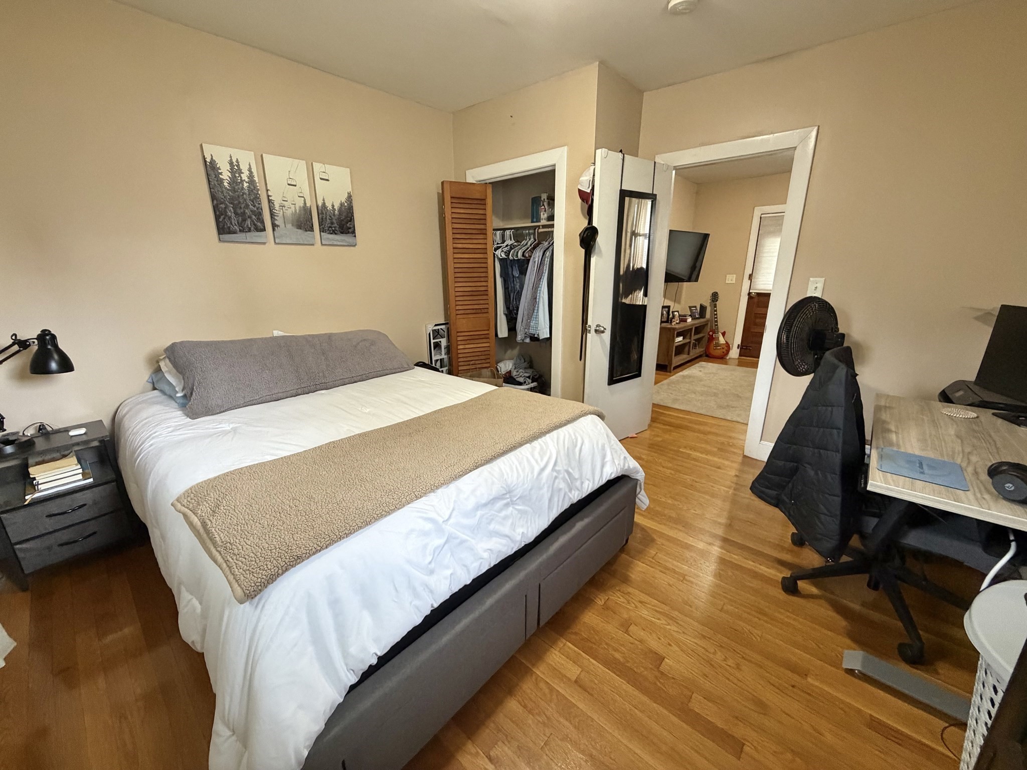 Bedroom with a gray upholstered bed, open closet, and desk beside a doorway to another room.