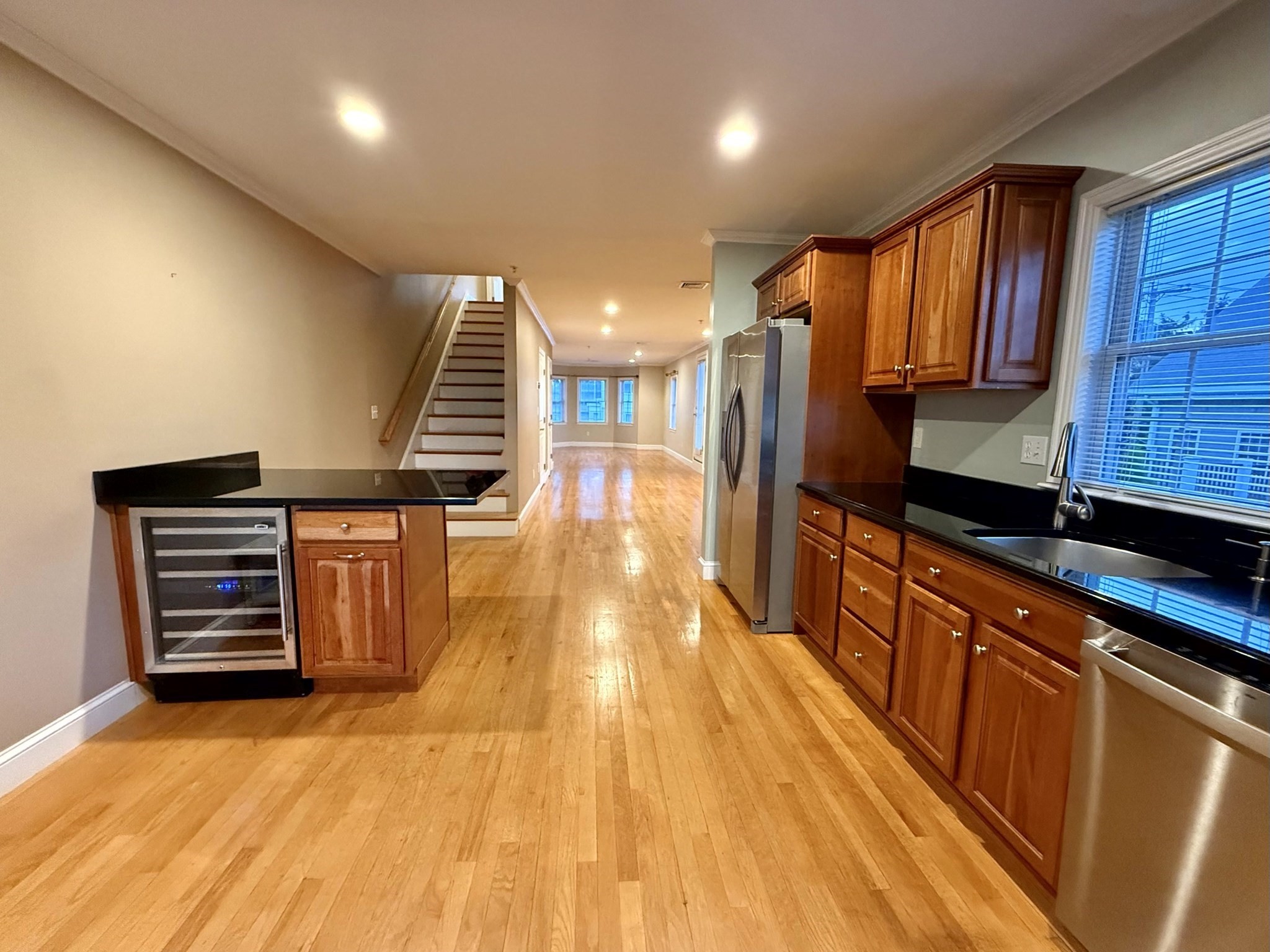 Open kitchen with wood floors, dark countertops, stainless steel appliances, and stairs leading to the living area.