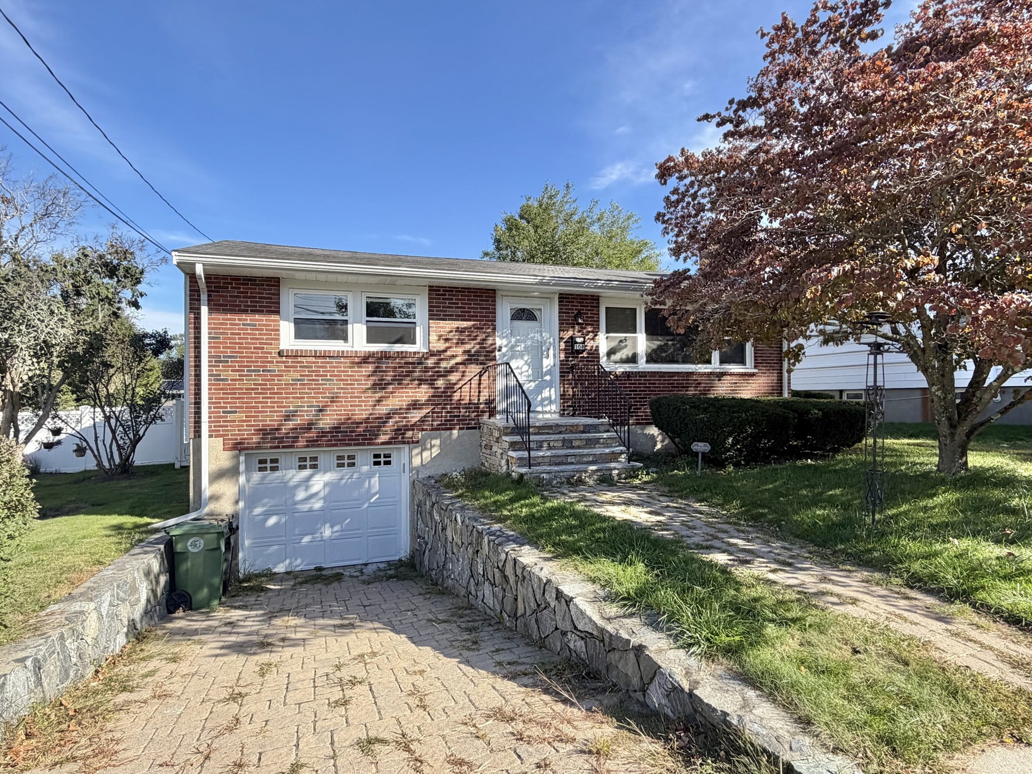 Red-brick home with a raised front entrance, lower-level garage, and stone retaining walls.