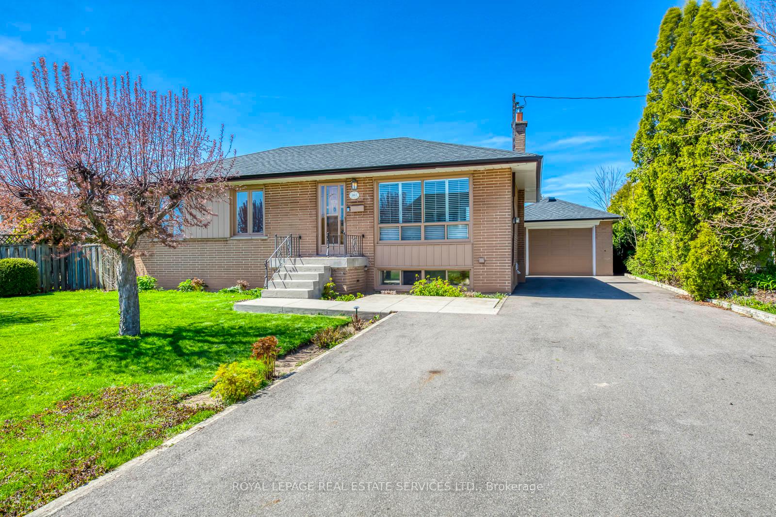 Brick bungalow with an attached garage, wide driveway, and flowering tree in the front lawn.