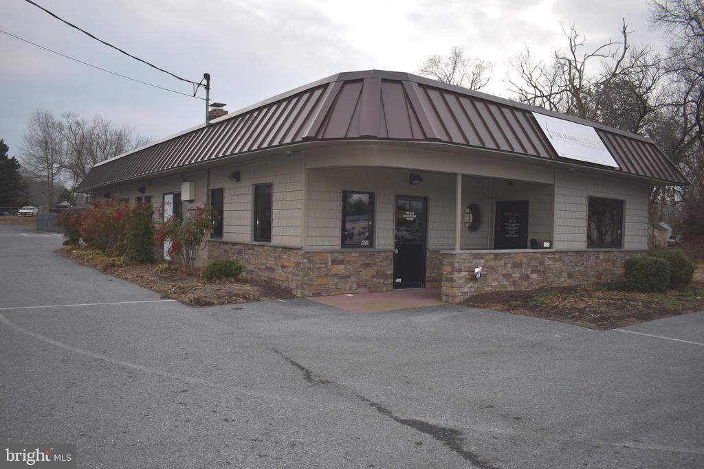Single-story commercial building with a brown metal roof and stone veneer beside a paved parking area.