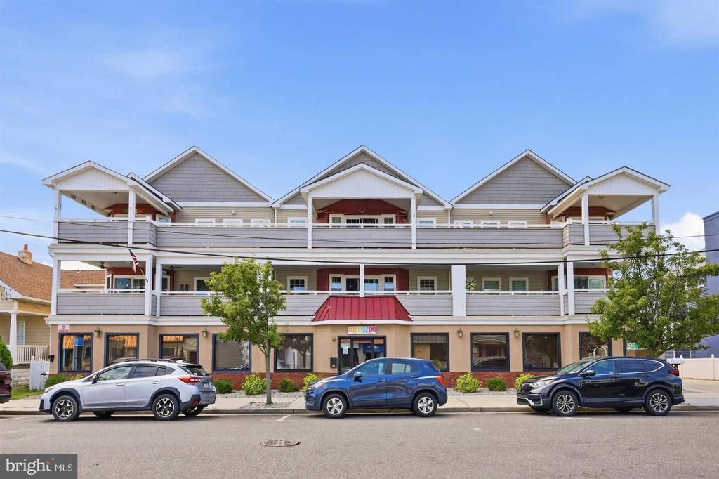 Multi-story shingle-sided building with wide balconies and ground-floor storefronts along a street.