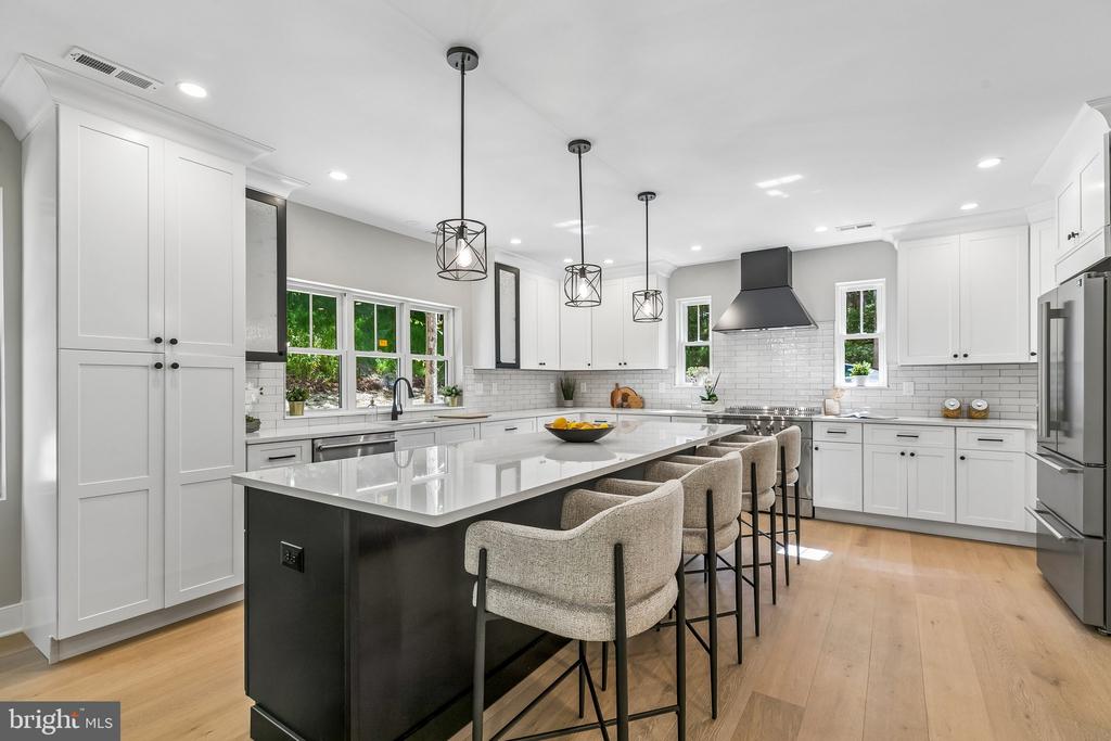 Bright white kitchen with a large black island, stone countertop, and upholstered counter stools.