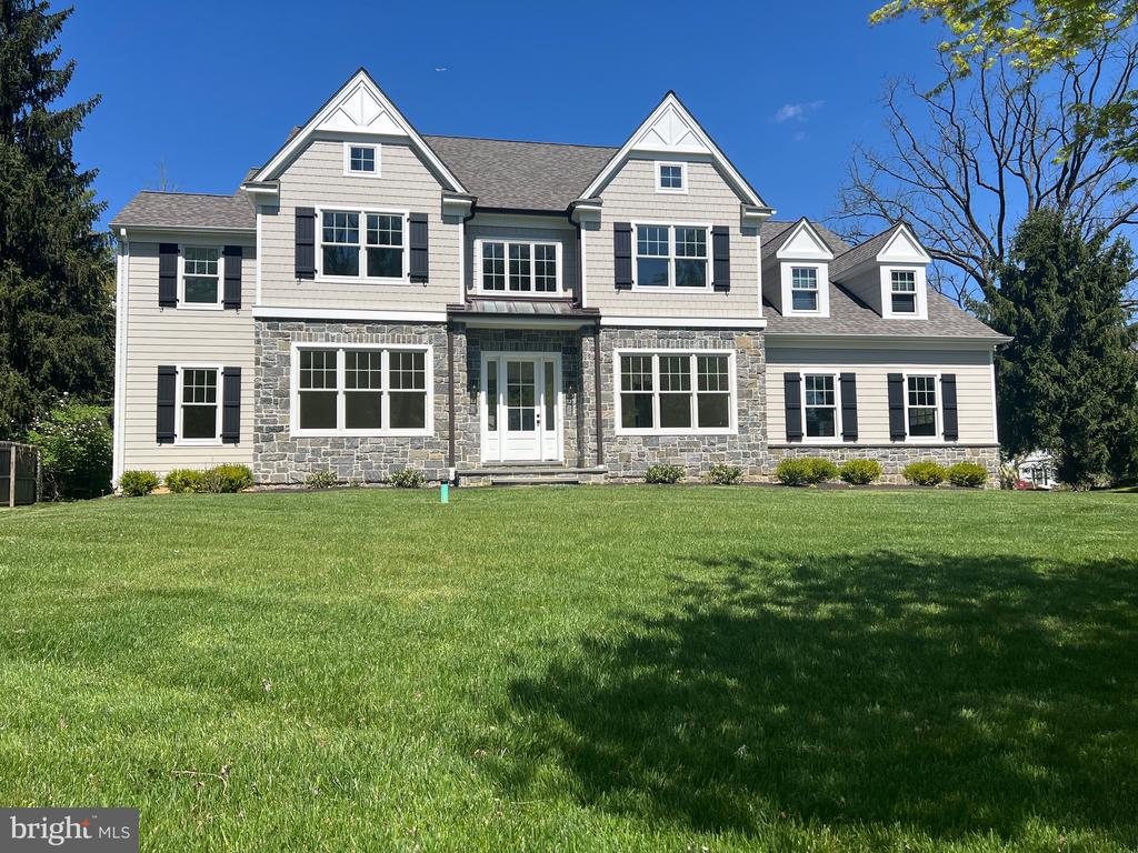 Two-story house with stone facade, multiple gables, and a wide green lawn.