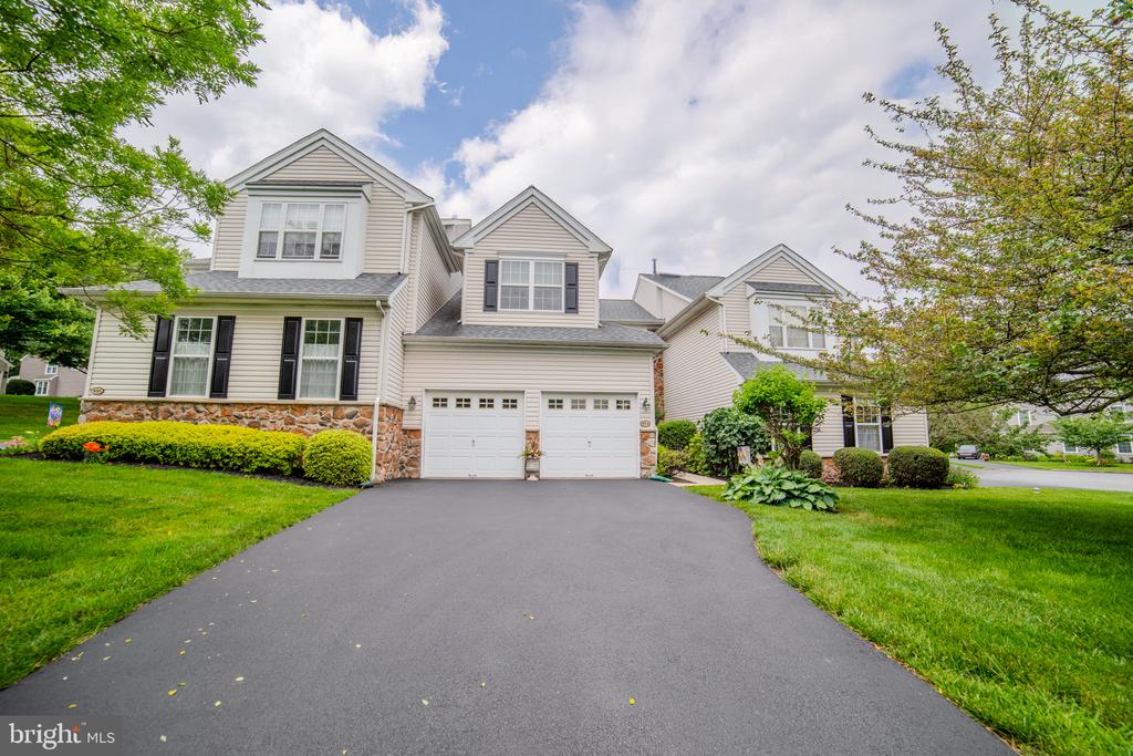 Two-story home with stone accents, black shutters, and a wide driveway leading to a two-car garage.