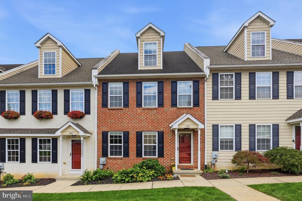 Red-brick townhouse at 306 with a red door, black shutters, and flower beds.