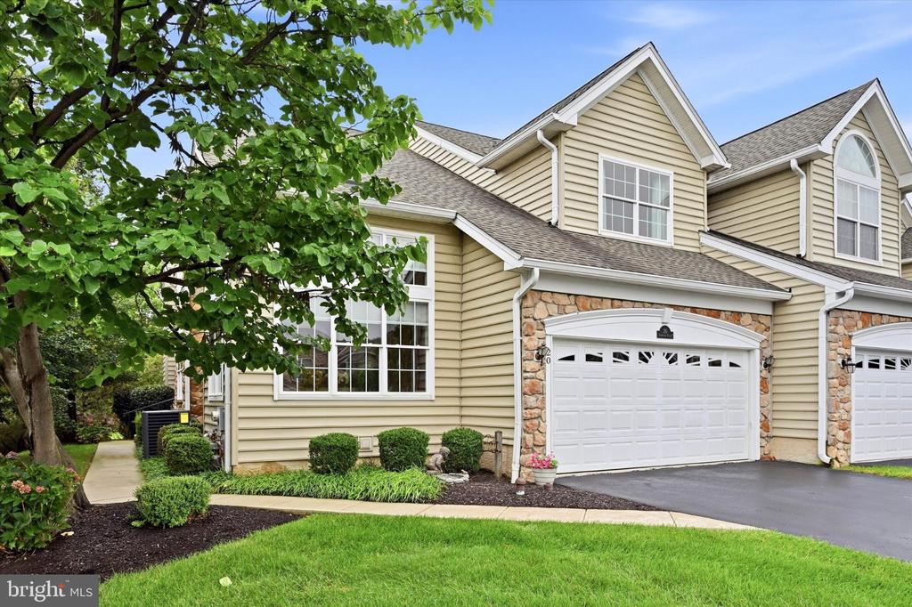 Beige-sided attached home with stone-trimmed garage, leafy tree, and landscaped front lawn.