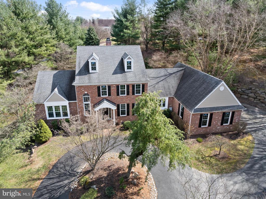 Aerial view of a two-story brick home with dormers and a curved driveway among mature trees.