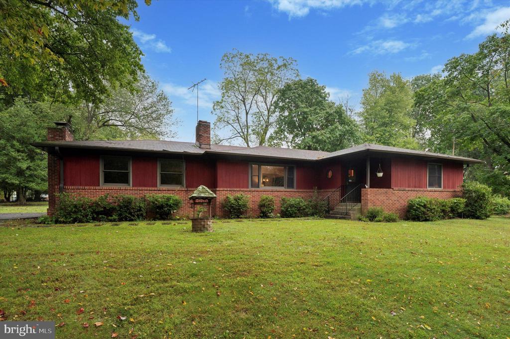 Single-story red ranch house with a brick facade, broad lawn, and mature trees.