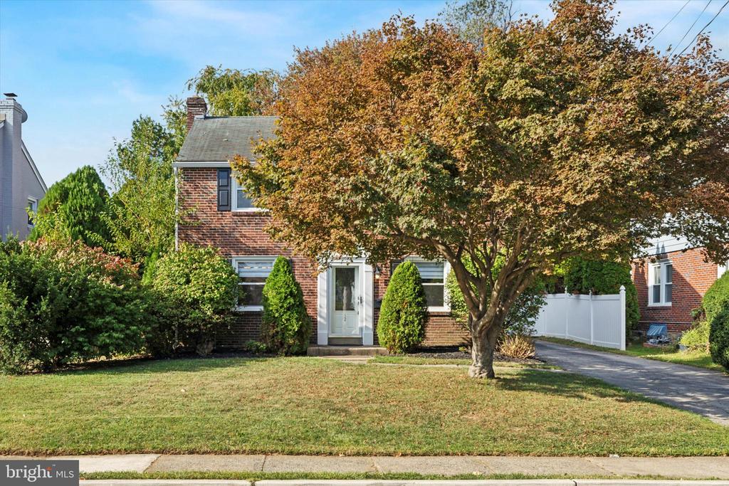 Two-story brick house beneath a broad autumn tree, with a front lawn and driveway.