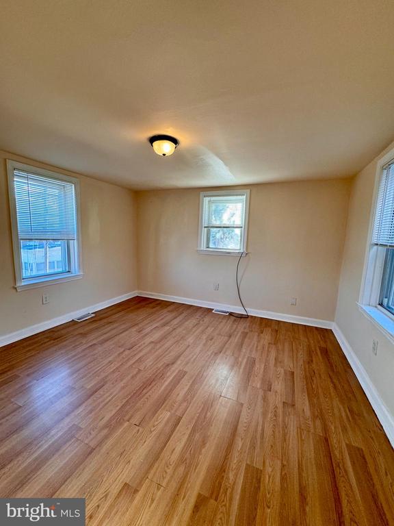 Vacant room with wood plank floors, beige walls, three windows, and a ceiling light.