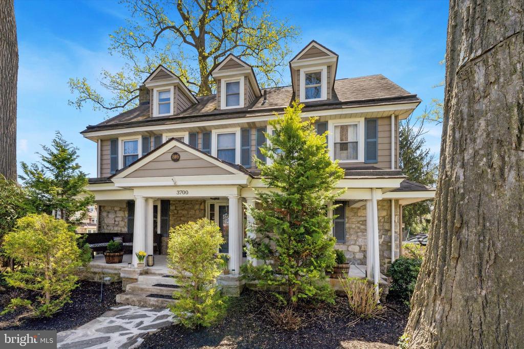 Two-story home with stone walls, blue shutters, three dormers and a columned front porch.