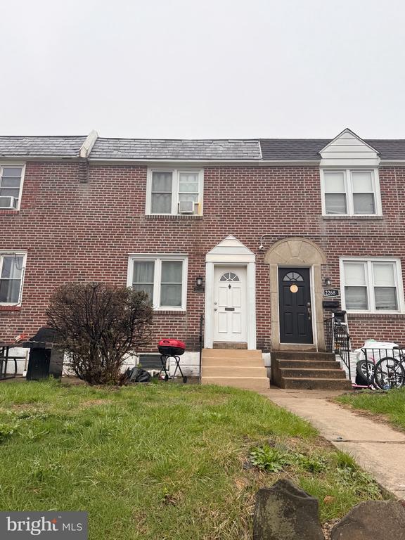 Red-brick rowhouse with white and dark front doors, steps, and a small grassy yard.