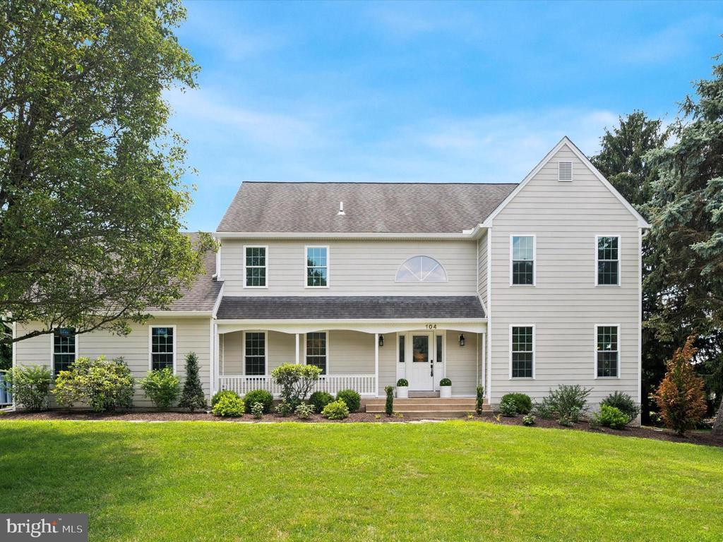 Two-story beige home with a covered porch, framed by mature trees and a broad green lawn.