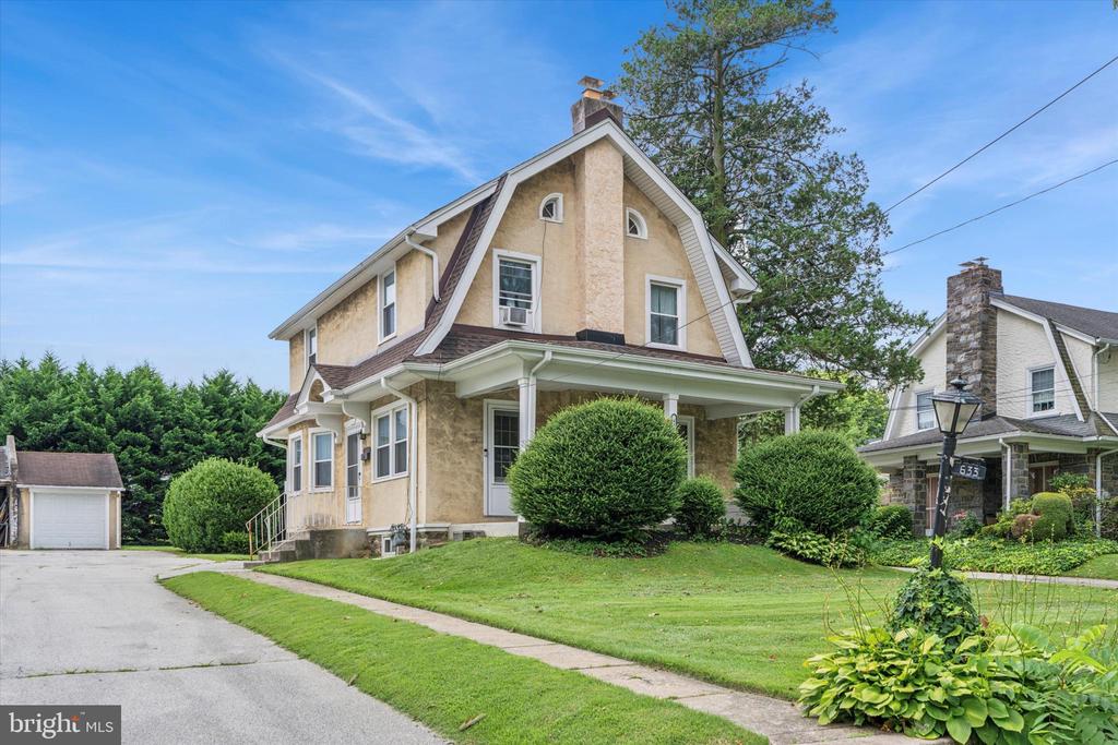 Tan stucco home with a steep gable, covered porch, and landscaped front lawn.
