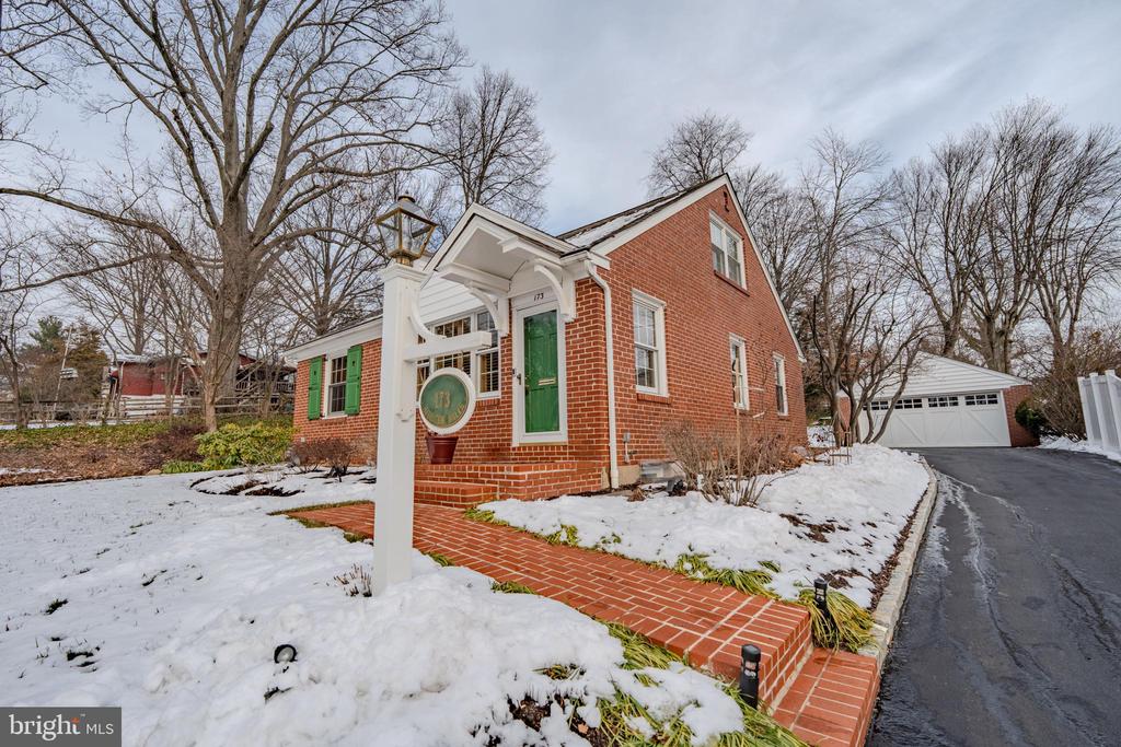 Red-brick house with a green front door, snow-covered yard, and detached garage.
