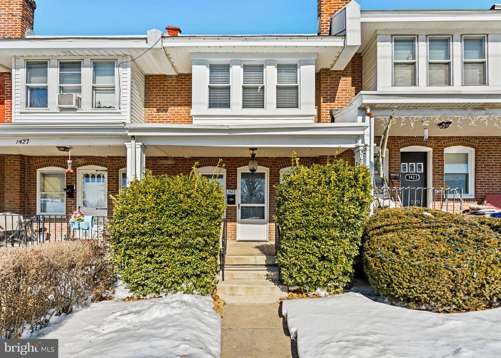 Brick row house with a central front entrance, clipped shrubs, and snow-covered ground.