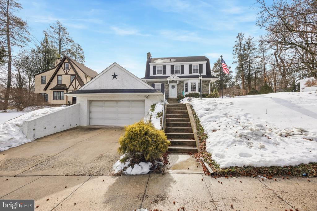Two-story house with a white garage, steep front steps, and an American flag amid snow.