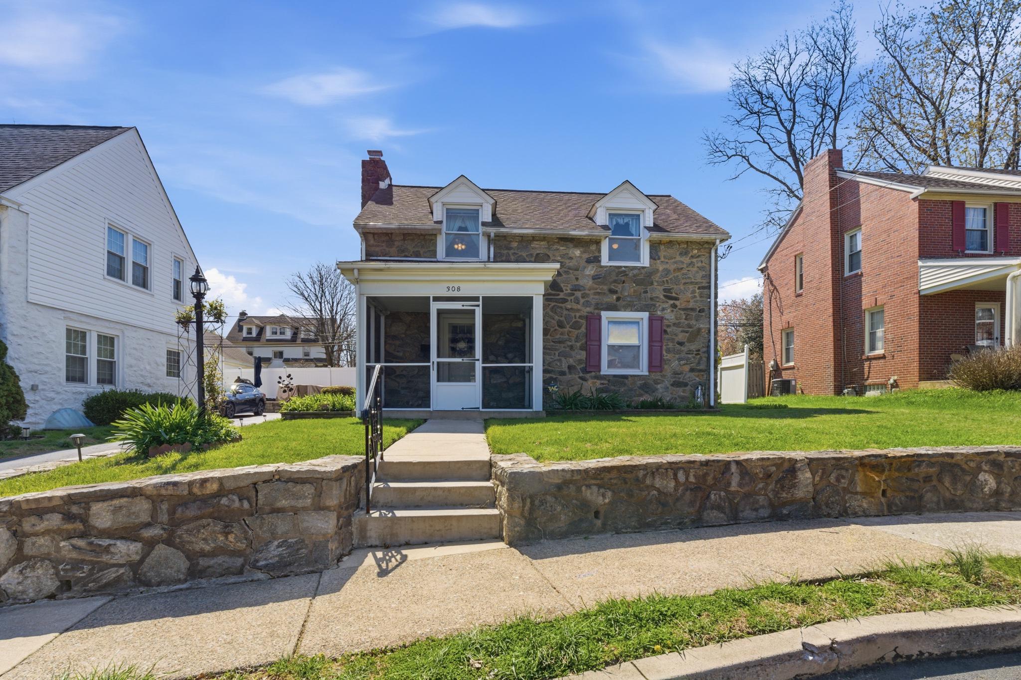 Stone-front house with dormer windows, covered entry, front steps, and a stone retaining wall.