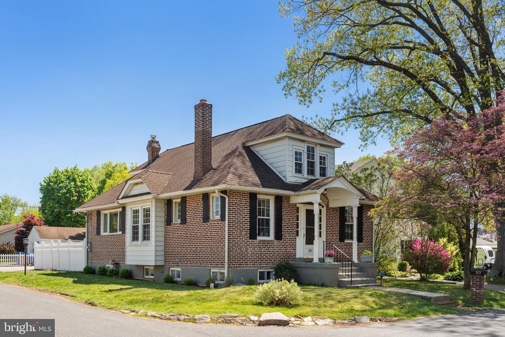 Red-brick house with white trim, two chimneys, and a small porch on a leafy corner lot.