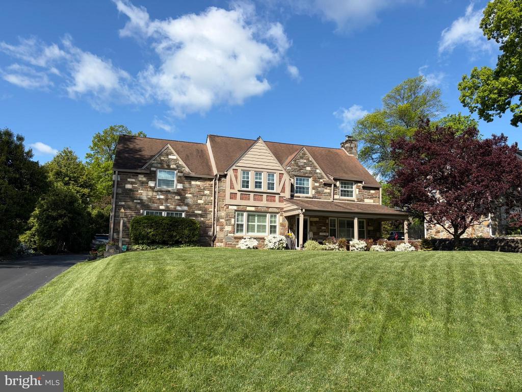 Stone house with a covered porch and broad, neatly mowed front lawn.