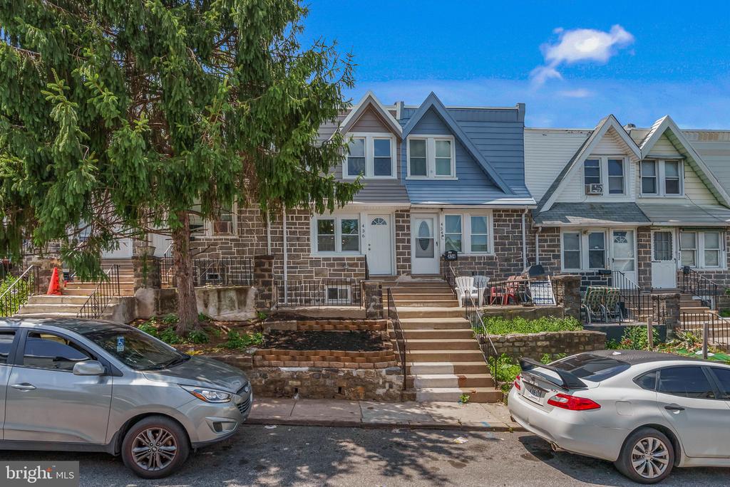 Stone-front row house with blue-gray gabled siding, front steps, and neighboring attached homes.