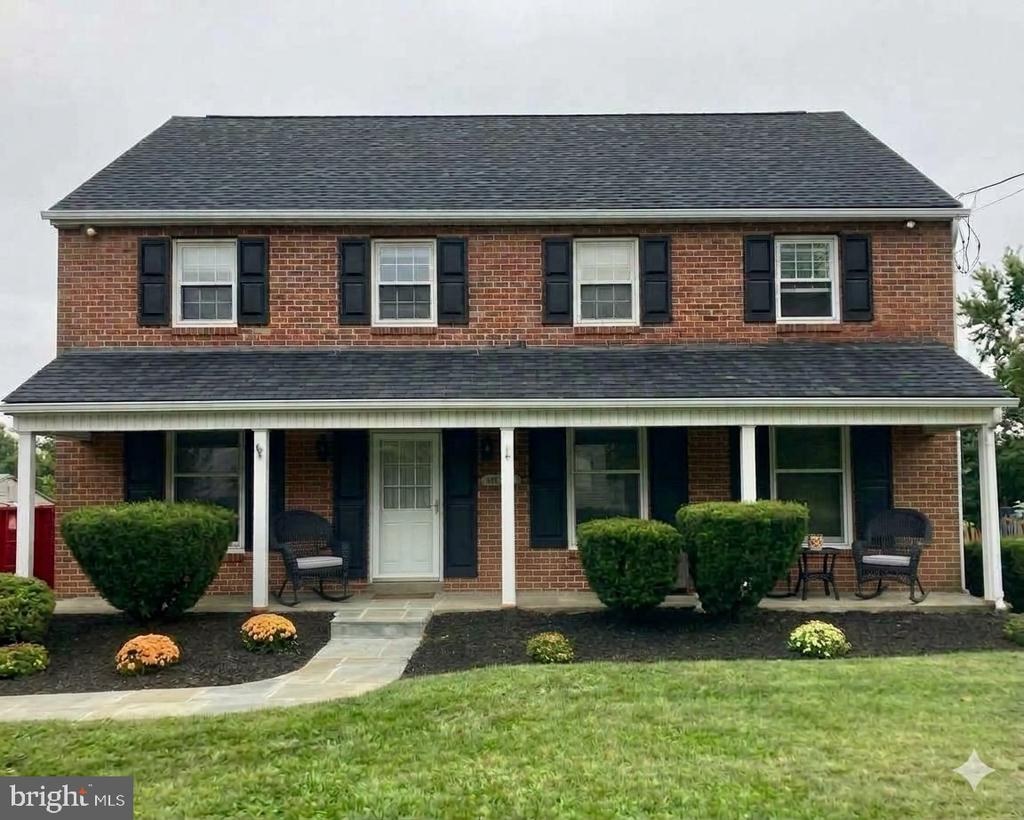 Two-story brick house with a covered porch, black shutters, and a curved front walkway.
