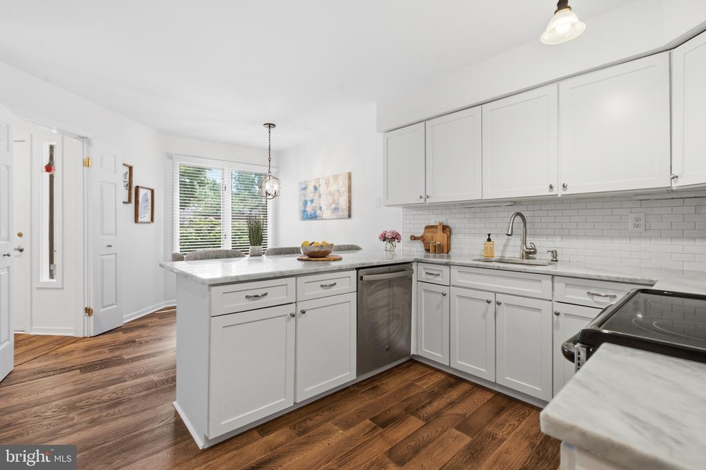 Bright white kitchen with a central island, subway tile backsplash, and dark hardwood floors.