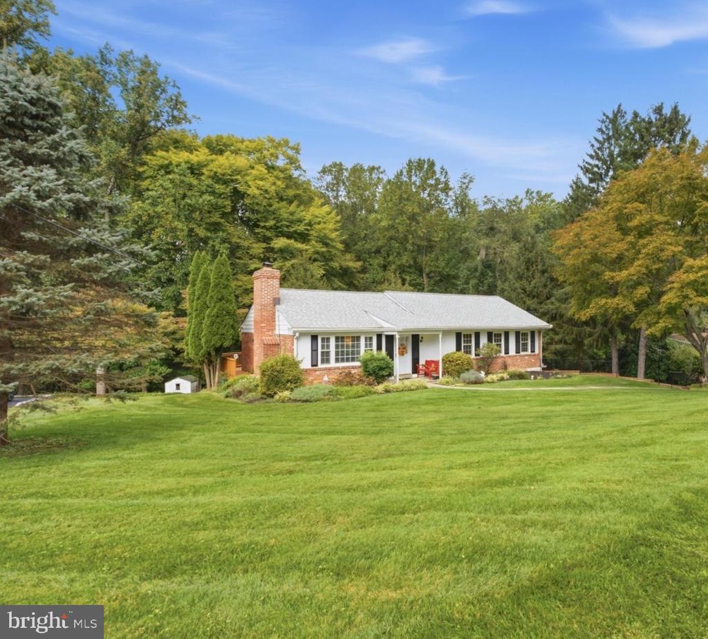 Single-story brick-and-siding house with a brick chimney, framed by mature trees beyond a broad lawn.