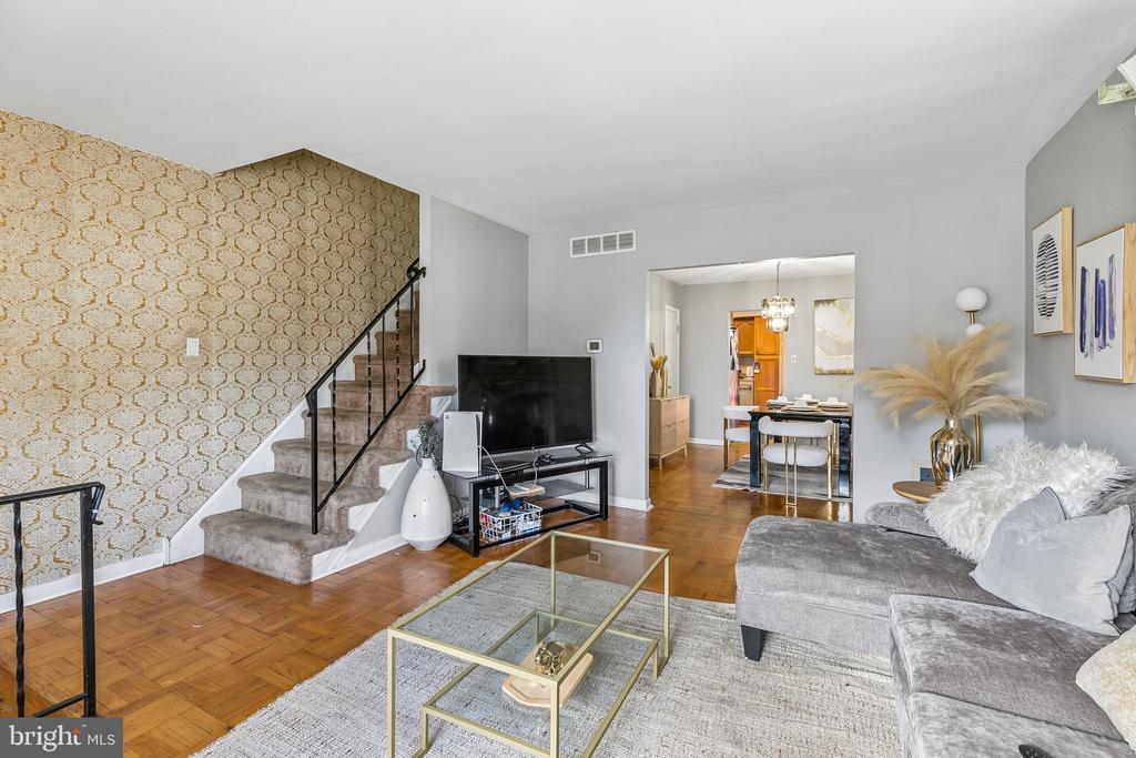 Living room with a gray sectional, parquet floors, patterned wallpaper, and a staircase.