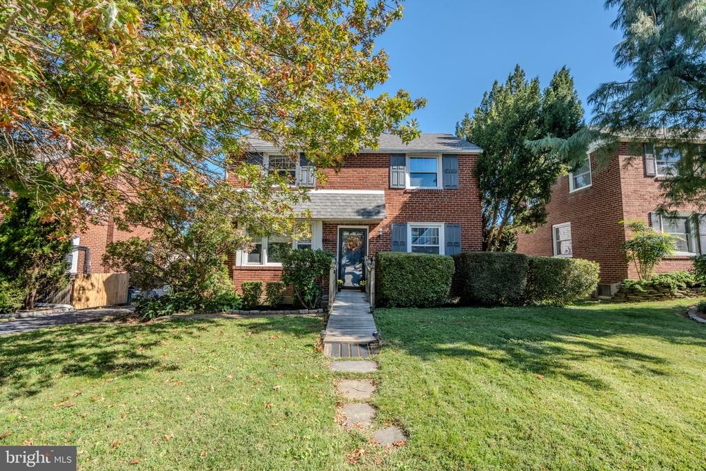 Two-story brick home with blue shutters, front walkway, lawn, and mature trees.