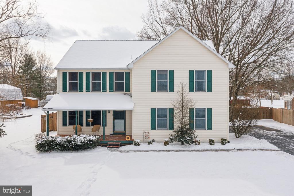 Two-story cream house with green shutters and a covered porch surrounded by snow.