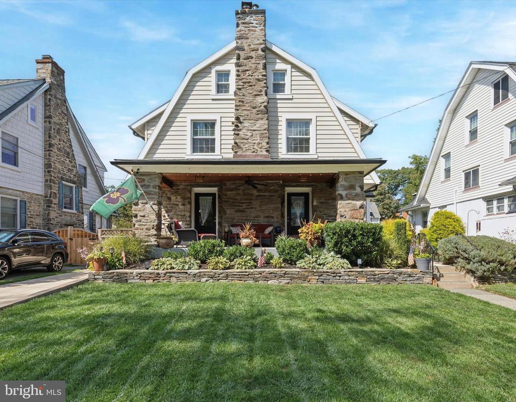 Home exterior with a stone chimney, gambrel roof, covered porch, and landscaped front garden.