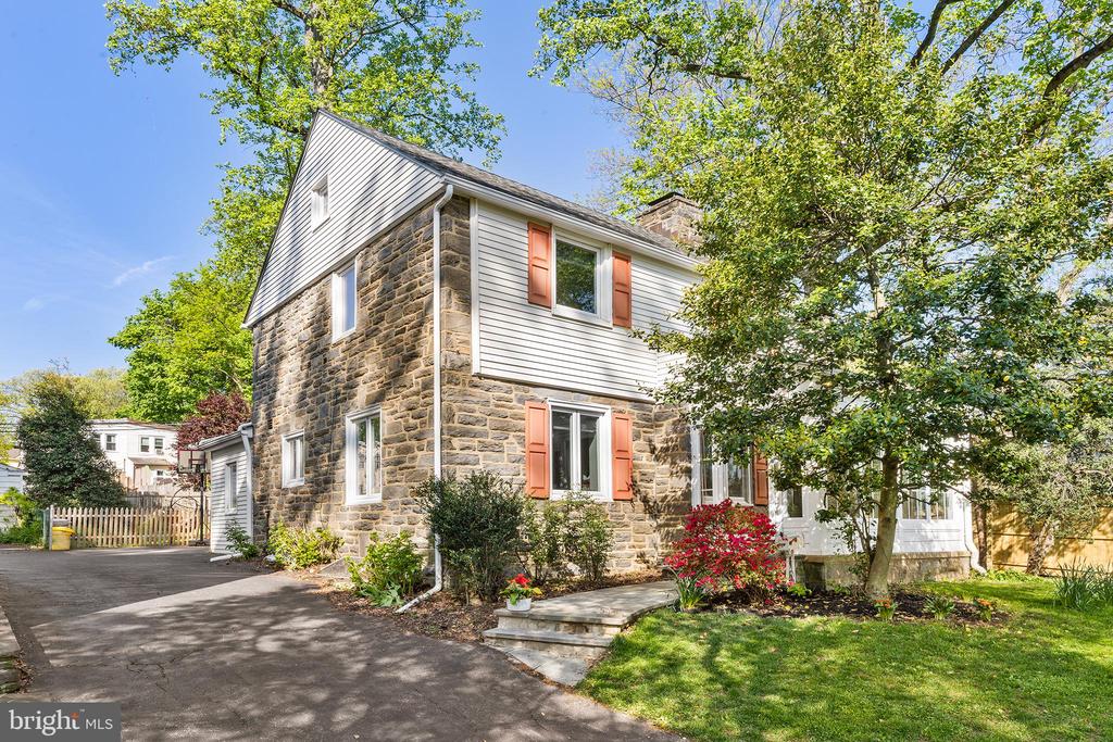 Two-story stone-and-siding house with coral shutters, a paved driveway, and mature trees.