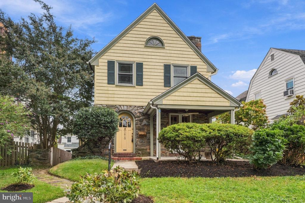 Yellow two-story home with a stone facade, covered porch, and landscaped front yard.