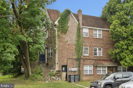 Two-story brick house covered with ivy, with mature trees and a gray SUV out front.