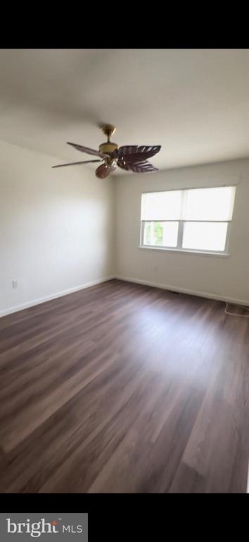 Empty room with wood-look flooring, a shaded window, and a leaf-blade ceiling fan.