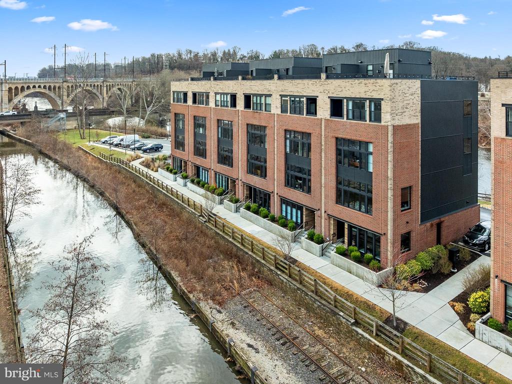 Modern brick apartments beside a creek and rail trail, with an arched stone bridge.