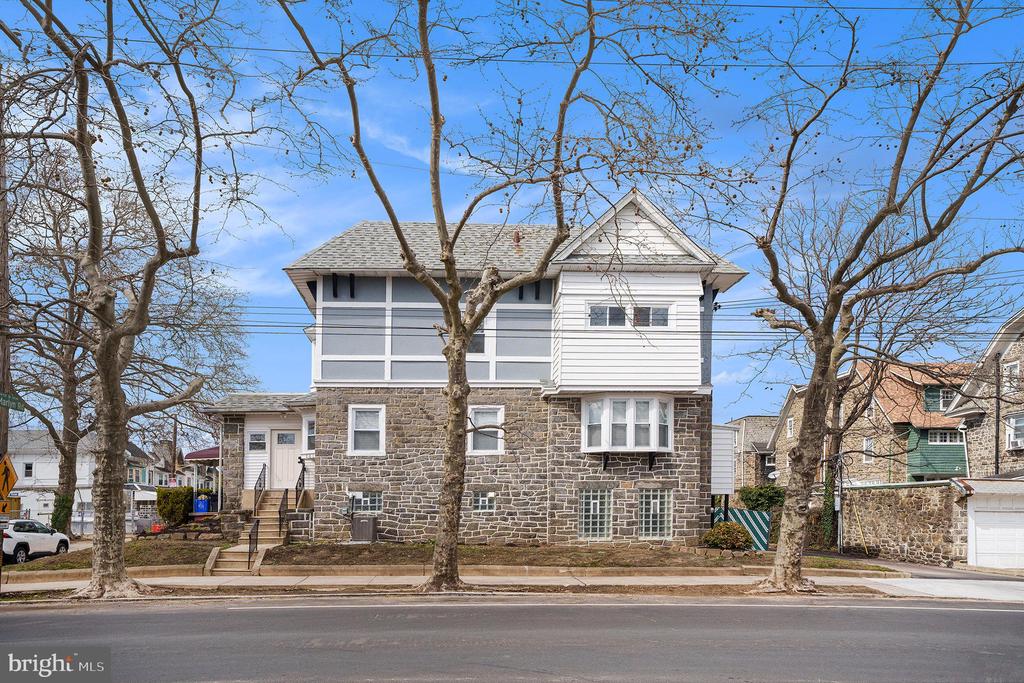 Two-story stone-and-white house behind leafless street trees.