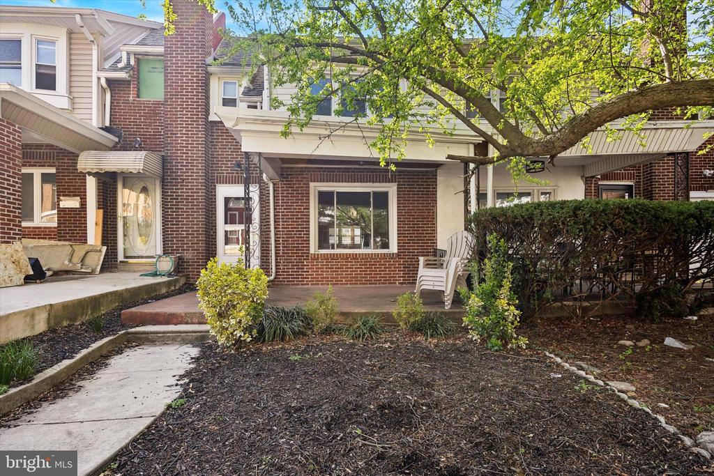 Brick townhouse exterior with a shaded patio, white chairs, and landscaped front yard.