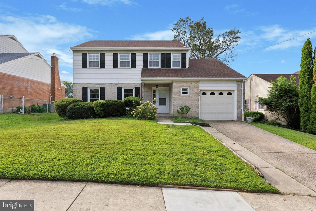Two-story white house with black shutters, brick lower facade, attached garage, and broad front lawn.