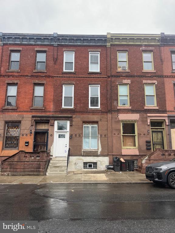 Three-story brick rowhouses with stone stoops along a wet city street.