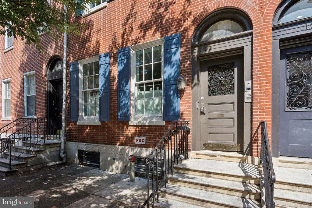 Red-brick rowhouse with blue shutters, arched doorways, and stone steps with iron railings.
