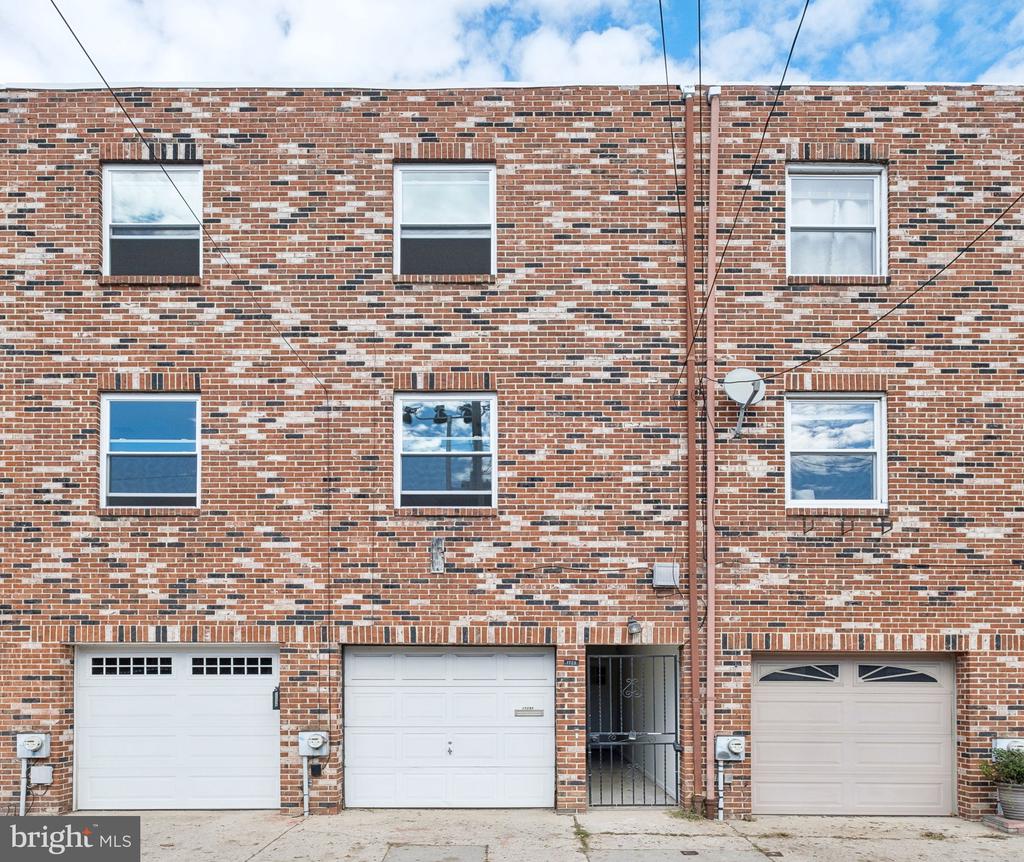 Brick rowhouse facade with multiple garage doors and a gated entrance.