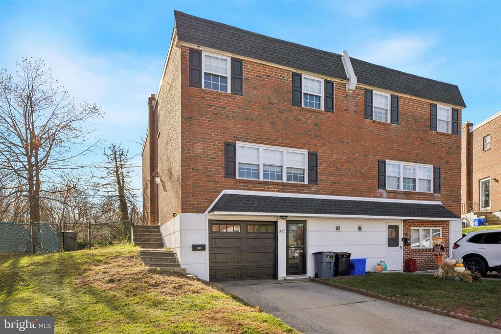 Three-story brick townhouse with an attached garage, front steps, and autumn decorations by the entrance.