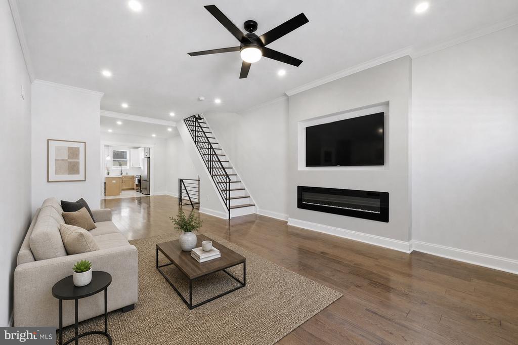 Living room with a light sectional, black metal staircase, and wall-mounted television above a linear fireplace.