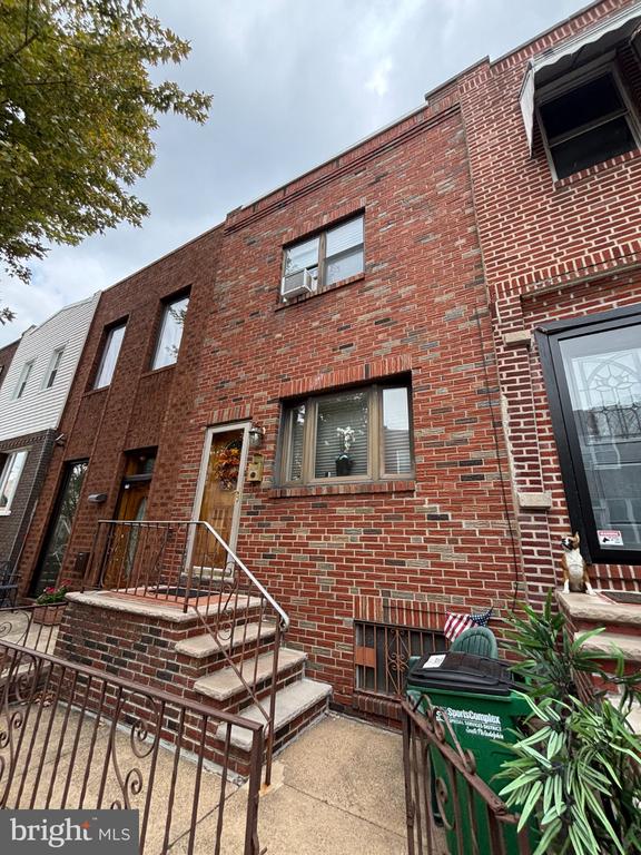 Red brick South Philadelphia rowhouse with a raised stoop and metal railings.